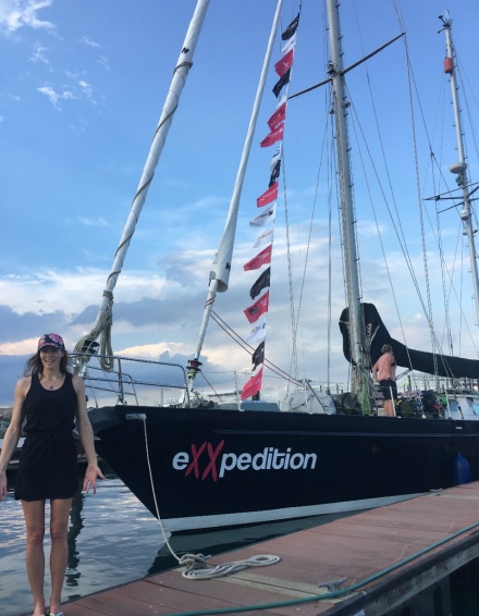 Zoom image: Alexa standing in front of eXXpedition sailboat from a distance