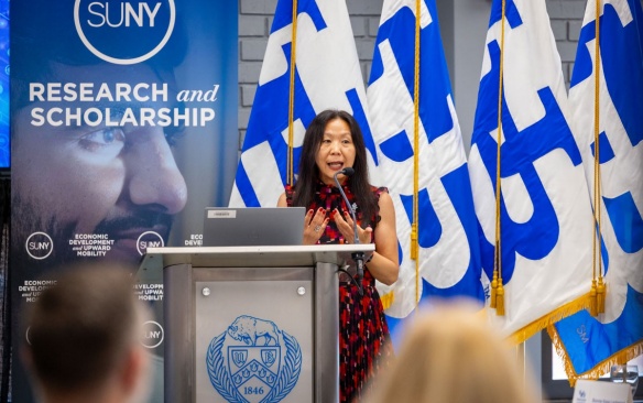 Christine Wang at a podium in front of UB flags. 