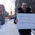 Photo of Jason Yip walking down a Buffalo sidewalk holding a posterboard saying "What do you think about kids and technology?". 