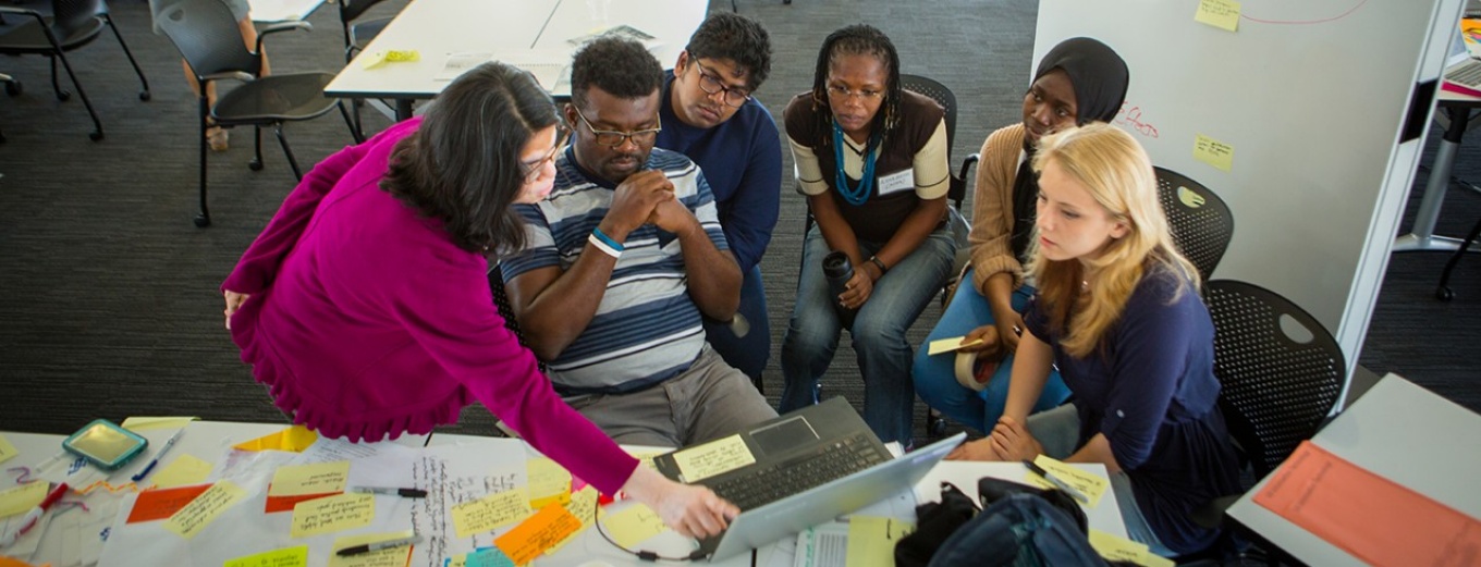 Students gathered around a laptop with adult supervision.