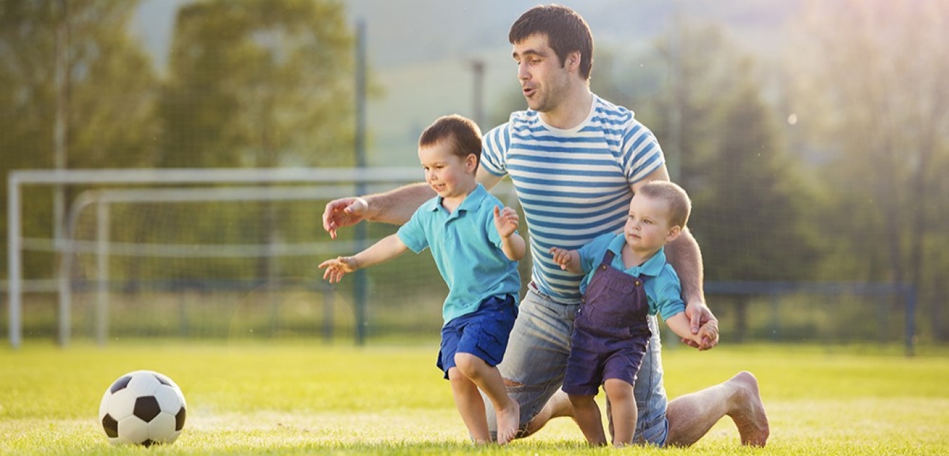 Dad coaching his sons on soccer field. 