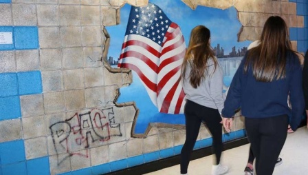 Schoolmates walking past a mural, showing a deconstructed wall, flag, "peace" written. 