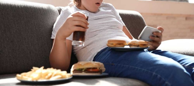 Overweight child sitting on couch eating burgers and drinking soda. 