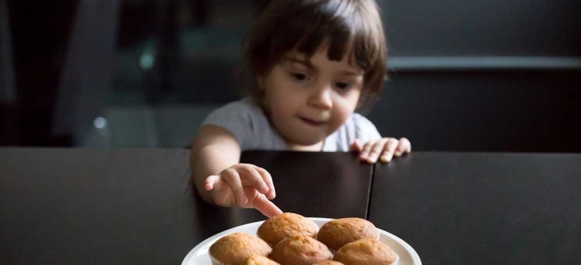 Child reaching for a plate of muffins. 