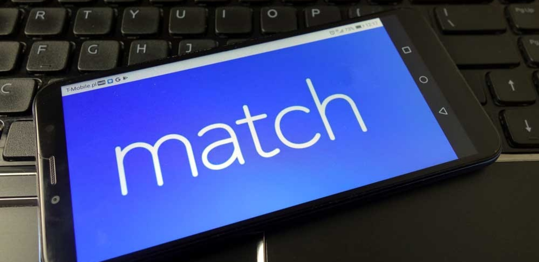 Image of a cell phone resing on a keyboard showing the word "match.".