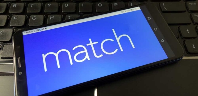 Image of a cell phone resing on a keyboard showing the word "match.". 
