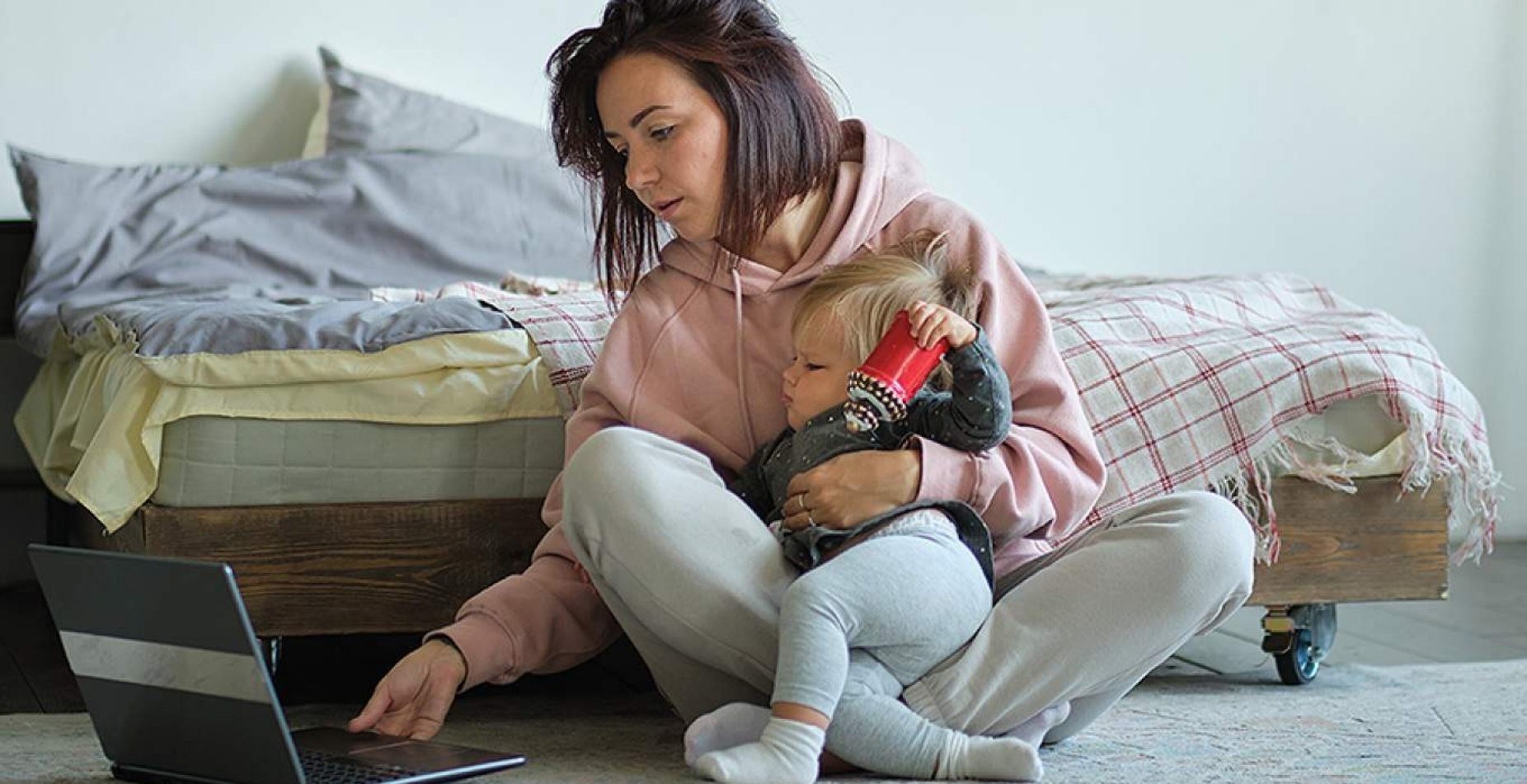 Mother wrestling a toddler while working on a laptop.