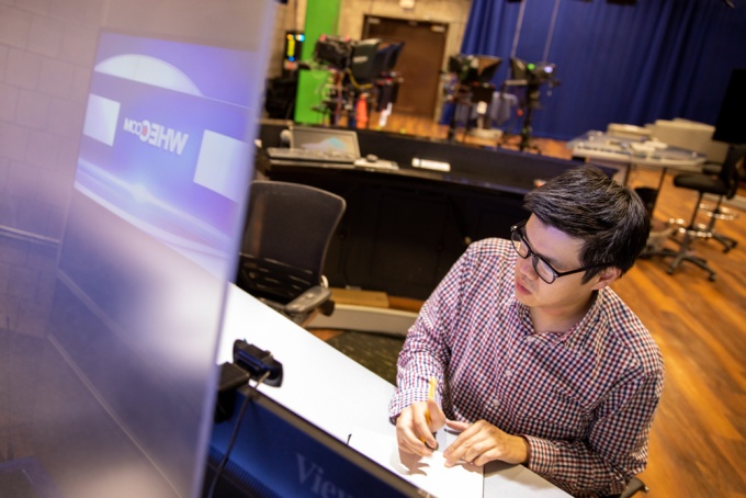 Picture of Carl Lam sitting at a news desk at News Channel 2 WGRZ in Buffalo, NY. 