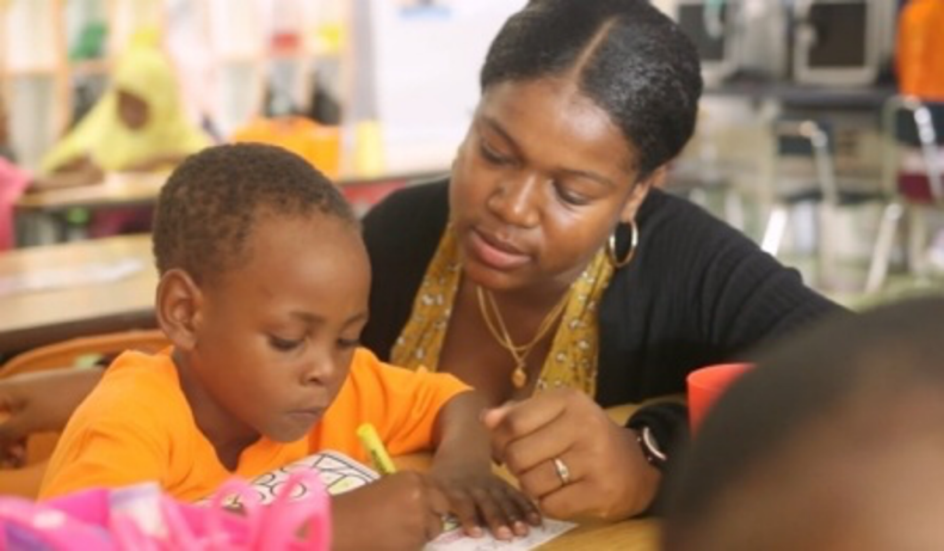 Image of a teacher working with a student in a classroom. 