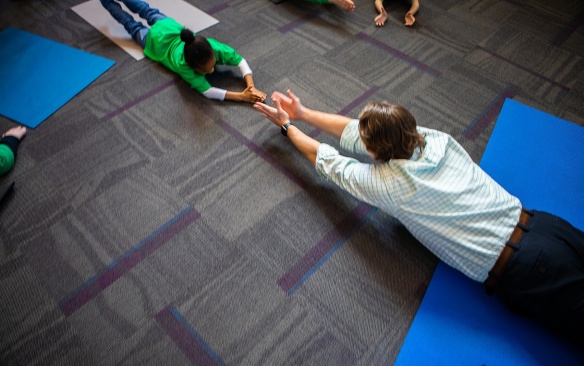 Zoom image: Teacher directing a child in a yoga pose. 
