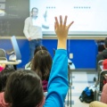 Image of children in a classroom raising their hands. 