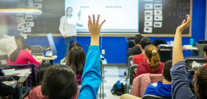 Image of students in a classroom with raised hands. 