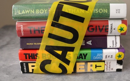 A stack of banned books with caution tape wrapped around them. 
