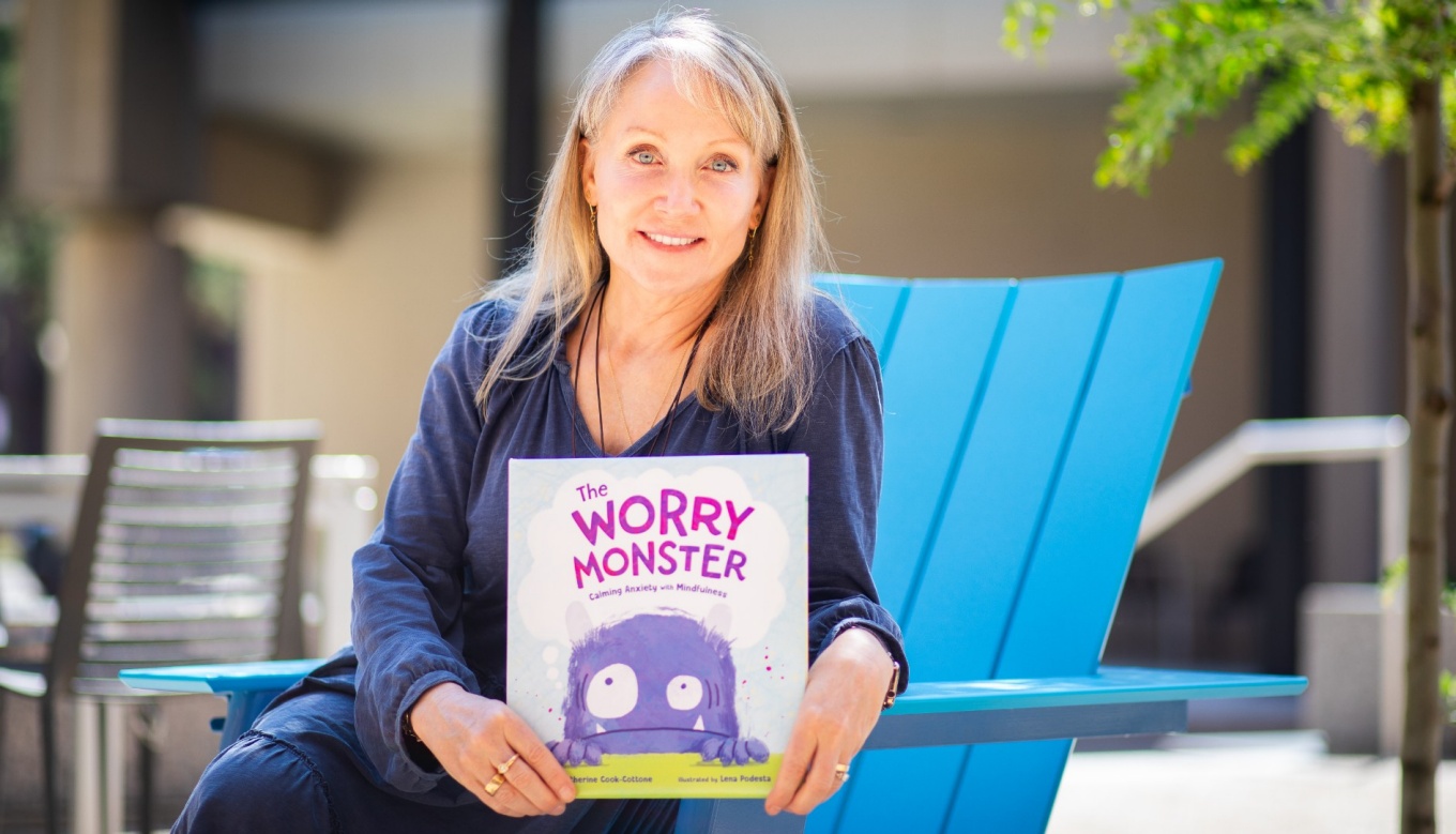 A portrait of Catherine Cook-Cottone, a professor of counseling, in the School and Educational Psychology, in the Graduate School of Education, taken in June 2024 in Paula’s Plaza on North Campus. She is photographed with her new book, “The Worry Monster.” Photographer: Meredith Forrest Kulwicki. 