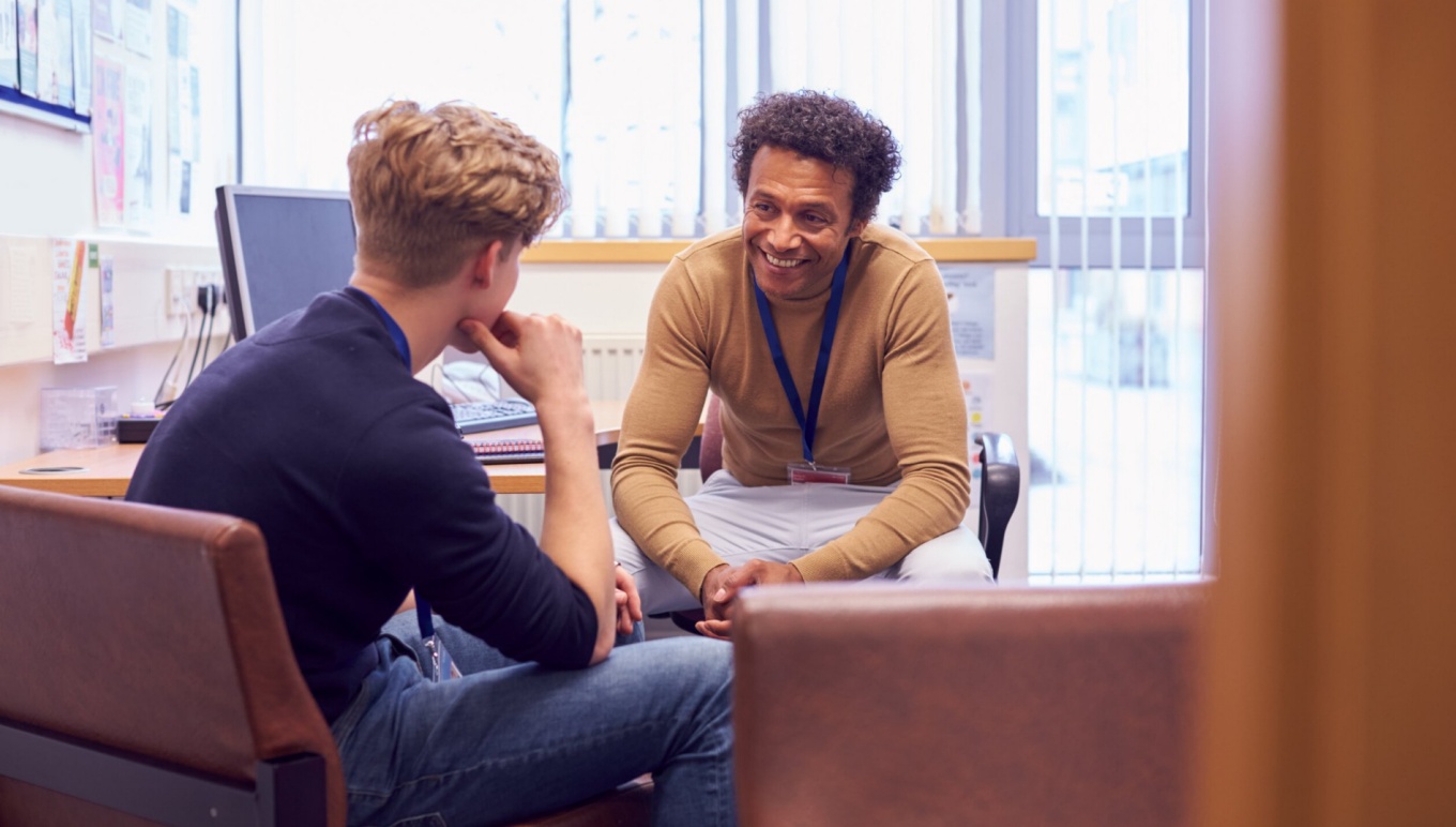 Male counselor and male patient sitting on chairs talking.