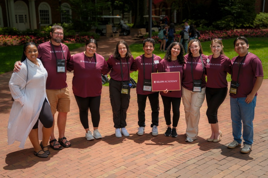 A group of Elon University students and staff pose together in matching maroon t-shirts.