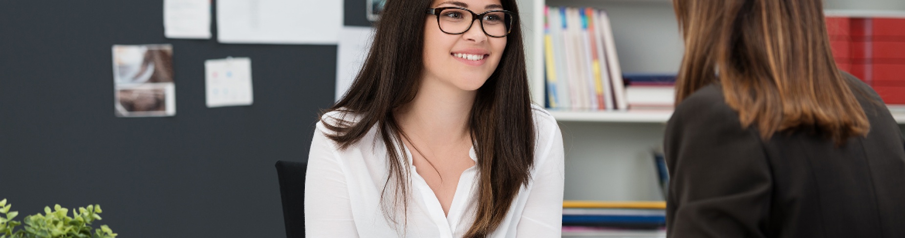 Two women meeting at a desk in a professional setting. 