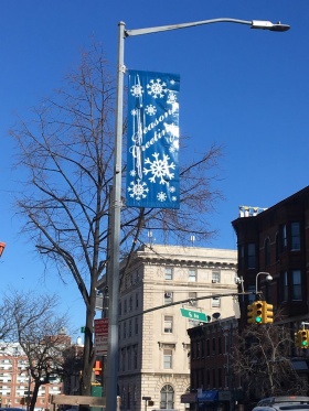 A blue banner with white snowflakes on it hanging on a street light. 