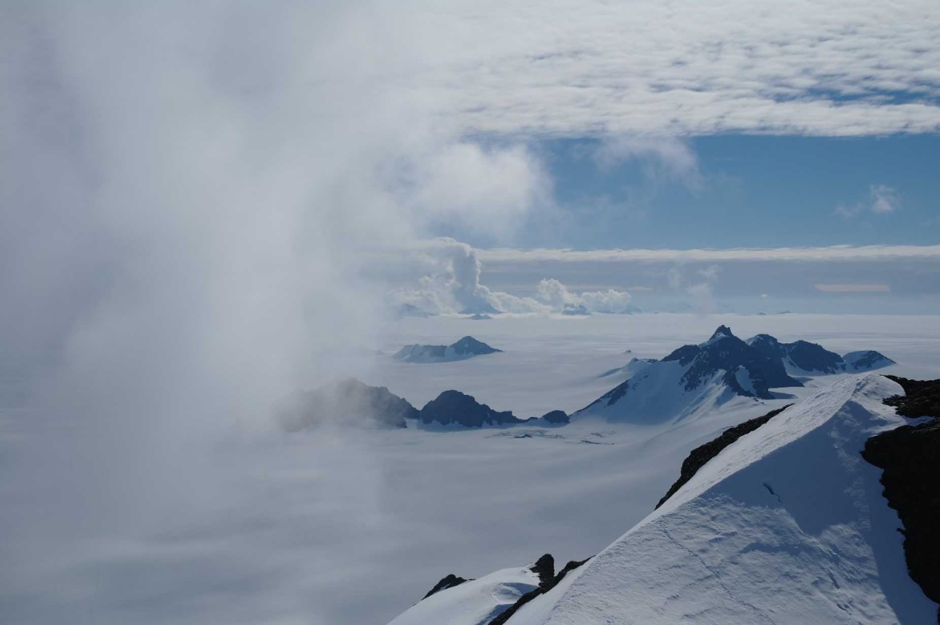 Clouds in a blue sky over an icy, mountainous landscape. 