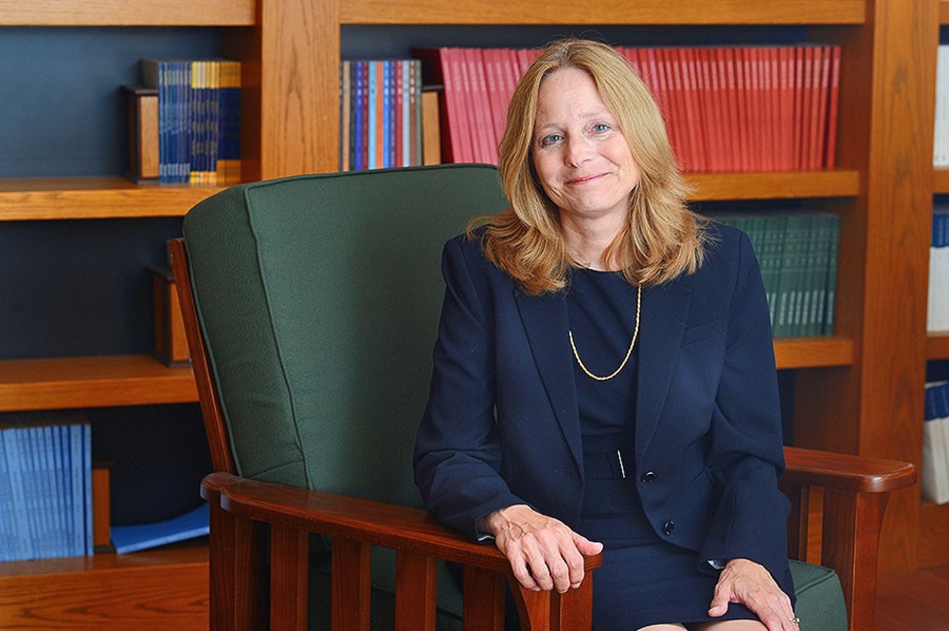 Nellie Drew sits in chair in front of books on a shelf. 