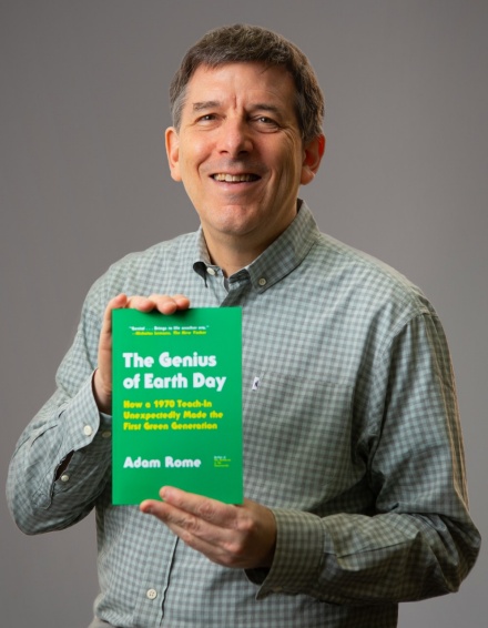 Adam Rome holding his book, "The Genius of Earth Day," with the title and information in white and yellow text on the front of a green cover. 