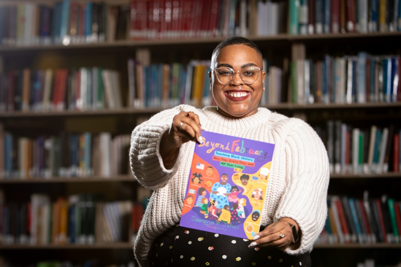 Dawnavyn James holds a picture book inside a library. 