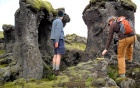 Two men climbing around lava pillars that are around the same height as they are. 