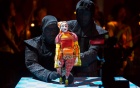 Two characters in black with a colorful puppet. 