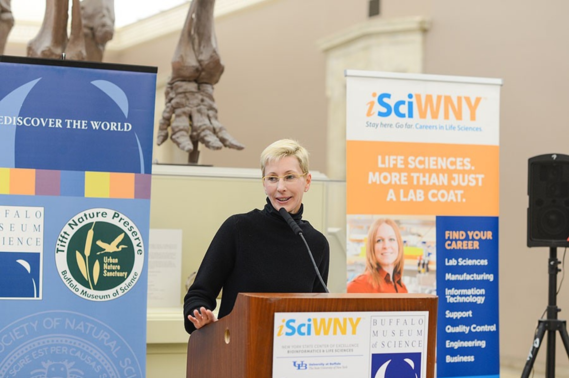 Norma Nowak stands in front of a podium surrounded by posters that promote the science, technology, engineering and math fields.