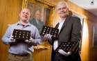Two men holding cases of coins. 