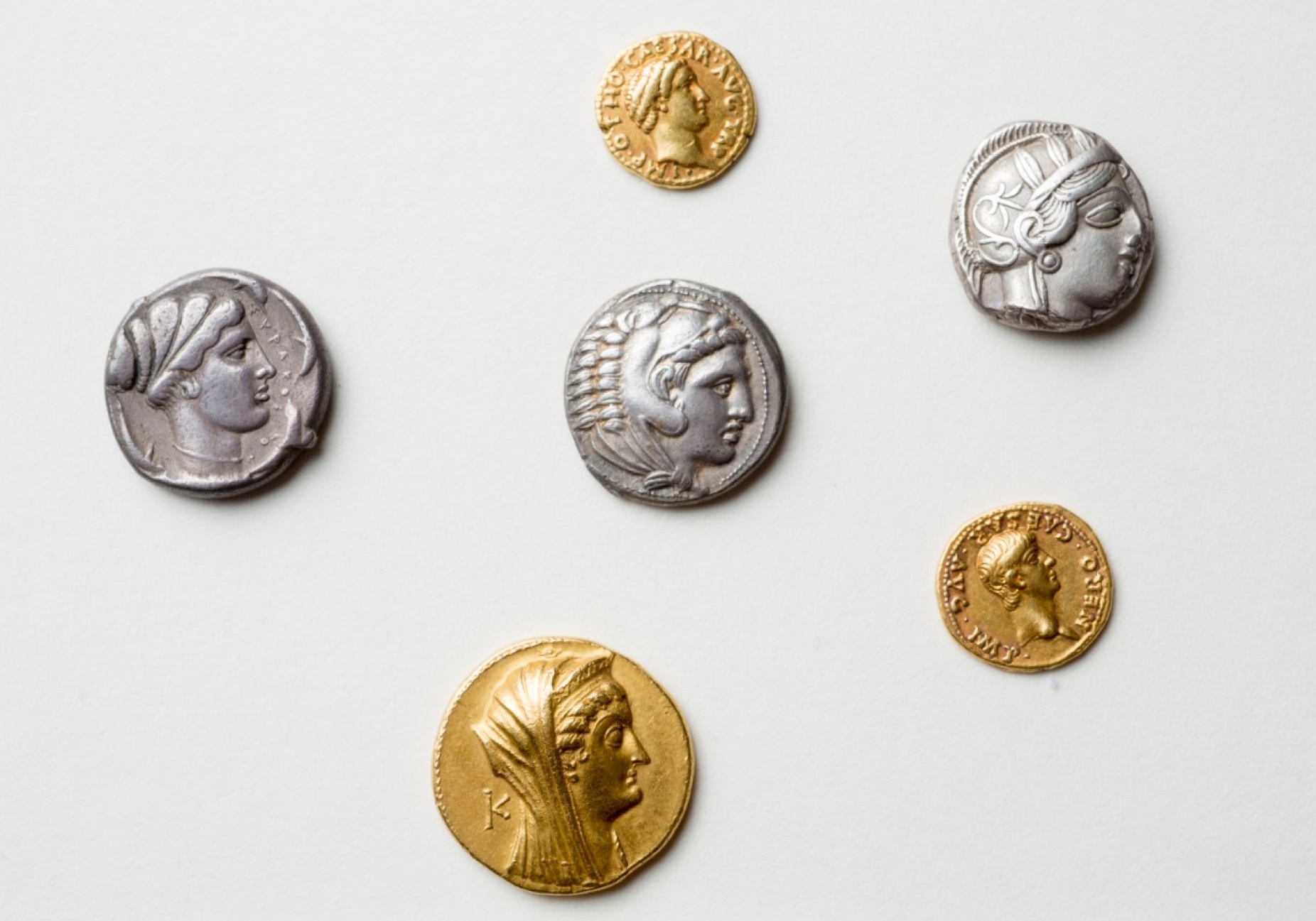 Zoom image: From top to bottom: a gold aureus of the Roman emperor Otho; a tetradrachm of Athens, showing the bust of the goddess Athena; a tetradrachm of Alexander the Great, showing Alexander dressed as the god Herakles; a silver tetradrachm of Syracuse (Sicily) showing the nymph Arethusa; a gold aureus of the emperor Nero; and a gold octodrachm of Arsinoe II. Credit: Douglas Levere 