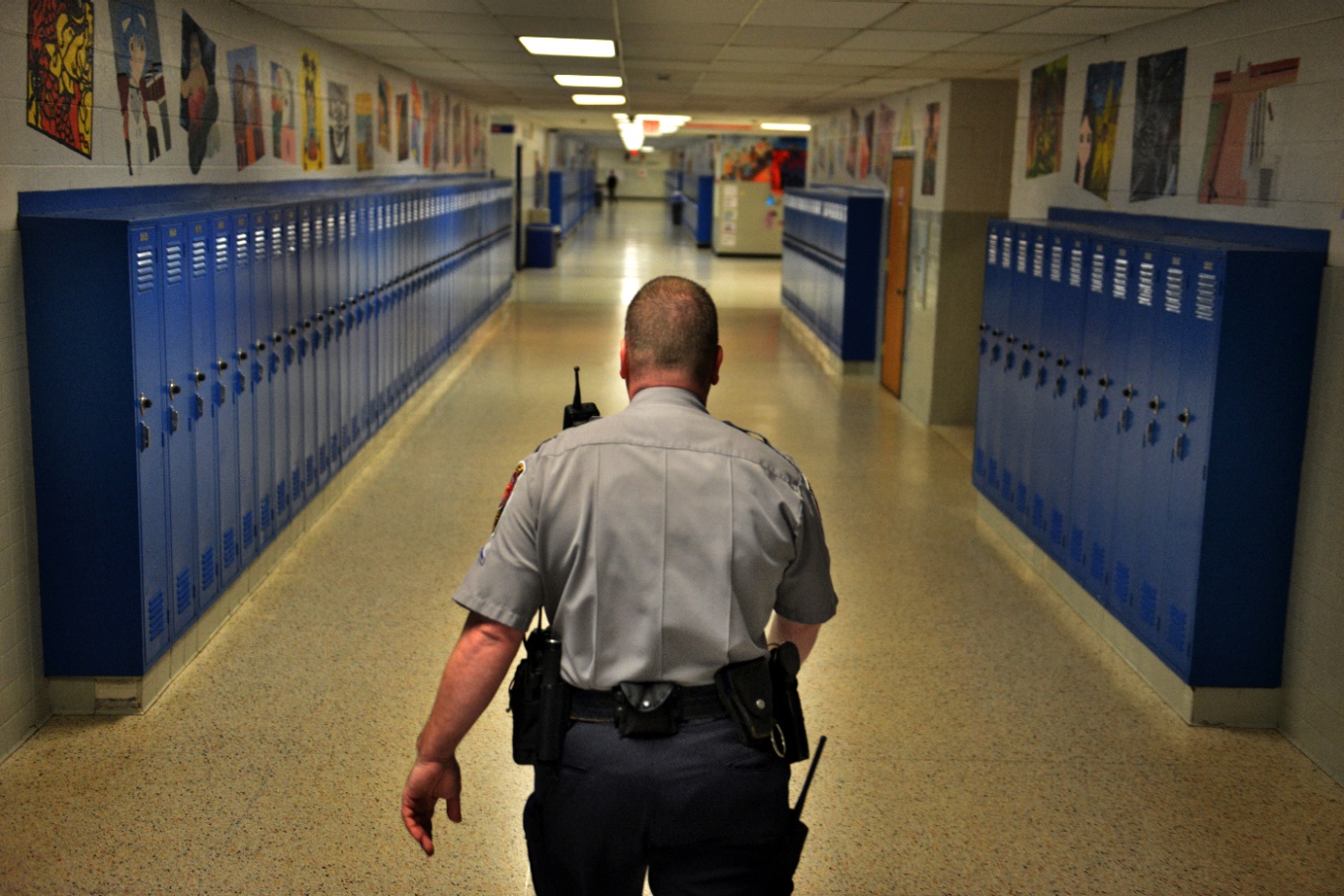 A security officer walking down a school hallway lined with lockers.