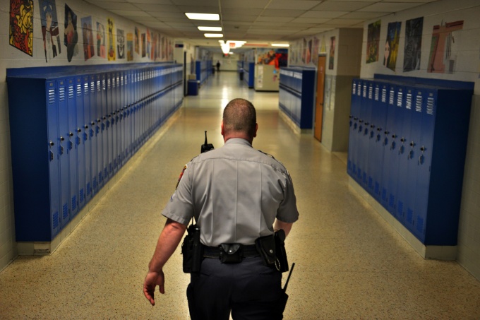 A security officer walking down a school hallway lined with lockers. 