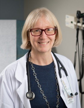 Janet Sundquist, MD, standing in front of exam table. 