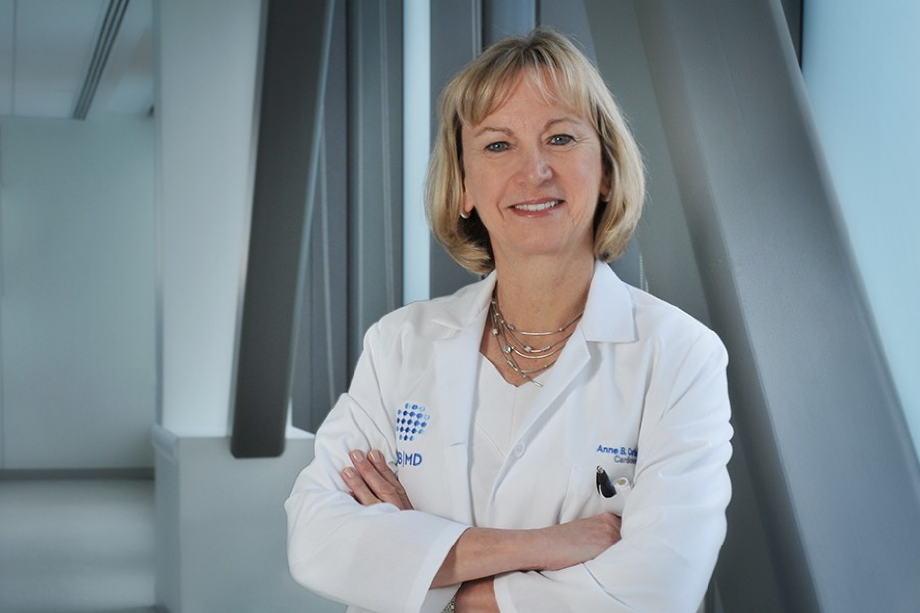 Anne Curtis in white coat standing in front of large windows.