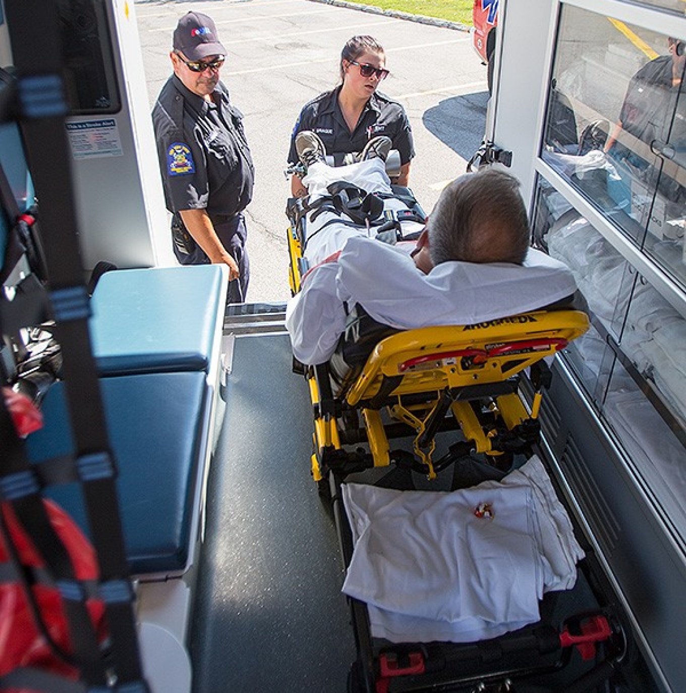 Photo of a man in a gurney being taken out of an ambulance. 