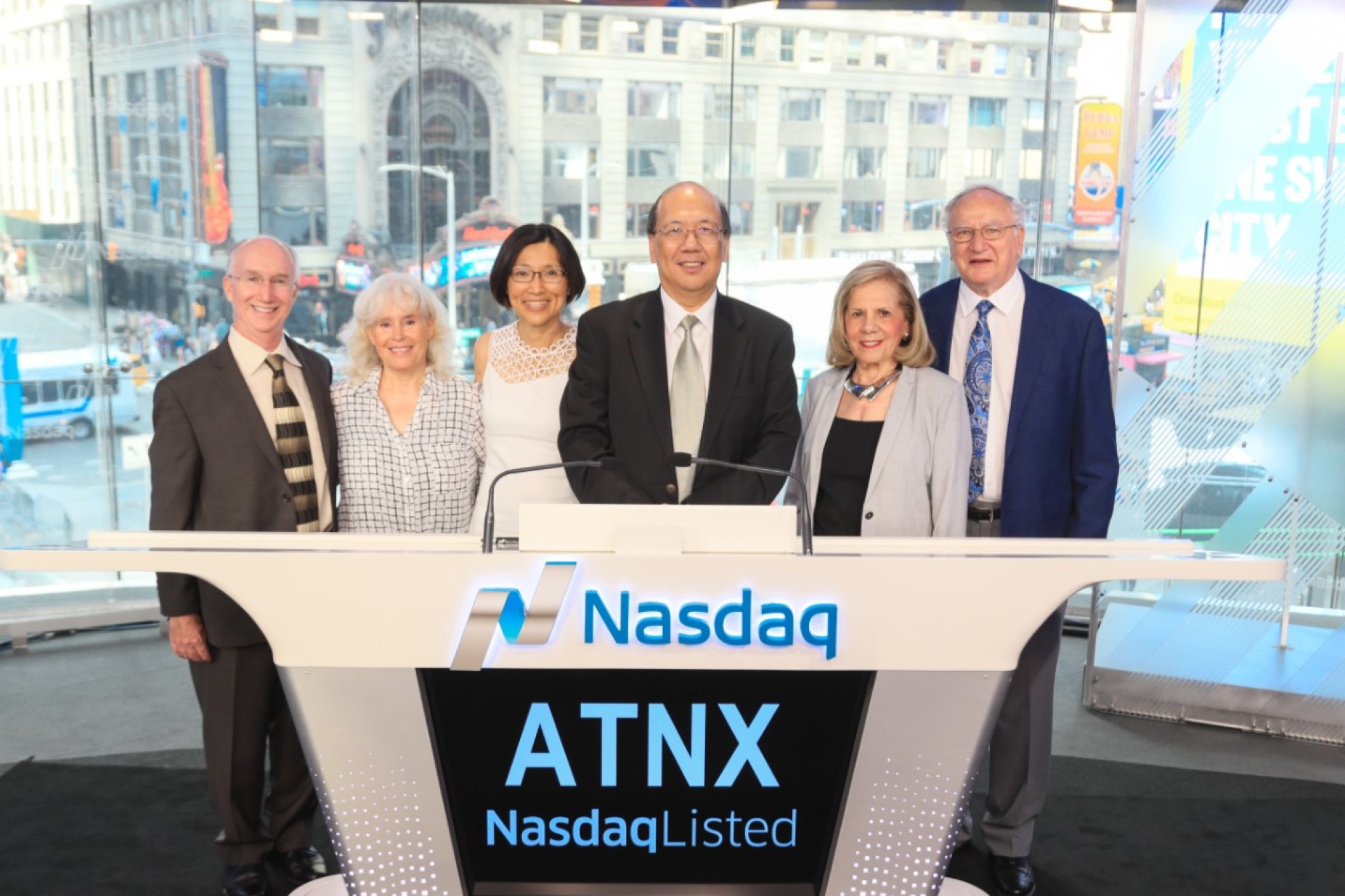 A group of people standing at a podium that reads "Nasdaq", with the letters ATNX displayed on the front. 