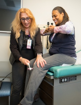 Weinstock-Guttman examines the reflexes of a patient in exam room. 