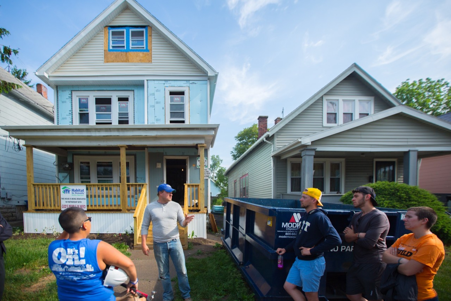 UB faculty member and students talking on the front lawn and in the driveway of a Habitat for Humanity house.