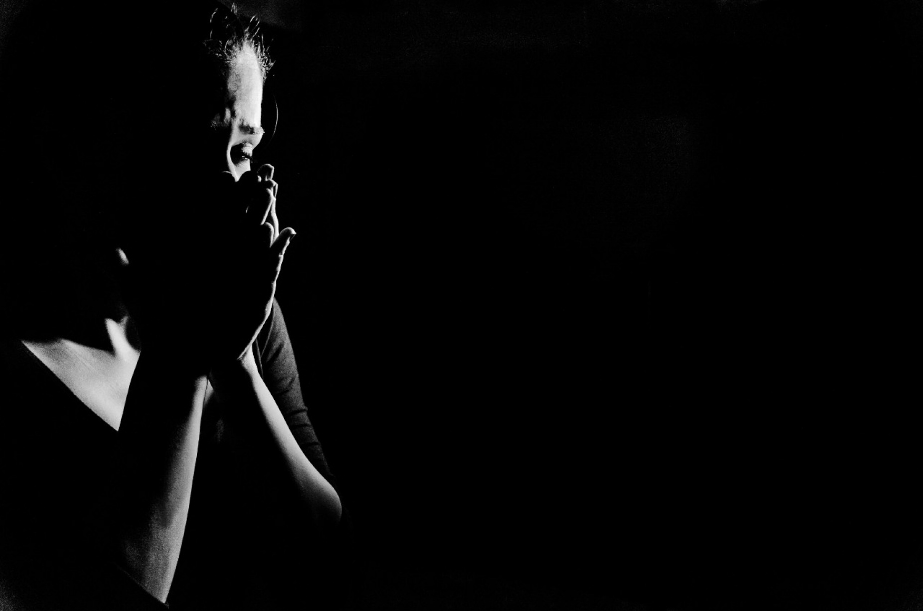 A woman sits in the dark with her hands over her face. 