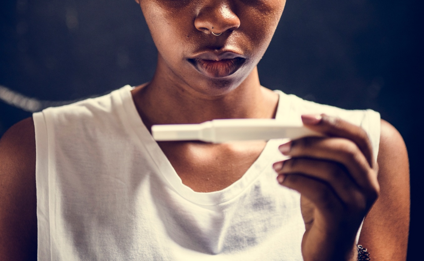 A young African-American woman holds a home pregnancy test.