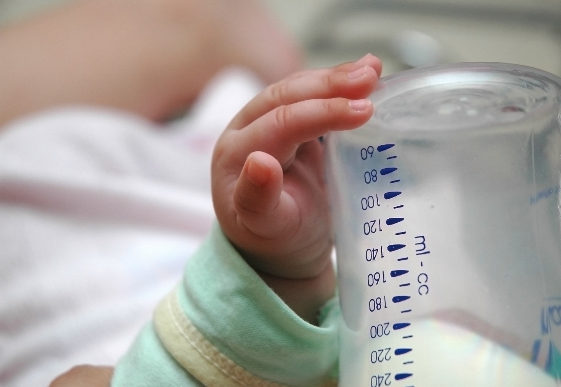 An infant's had rests on a baby bottle. 