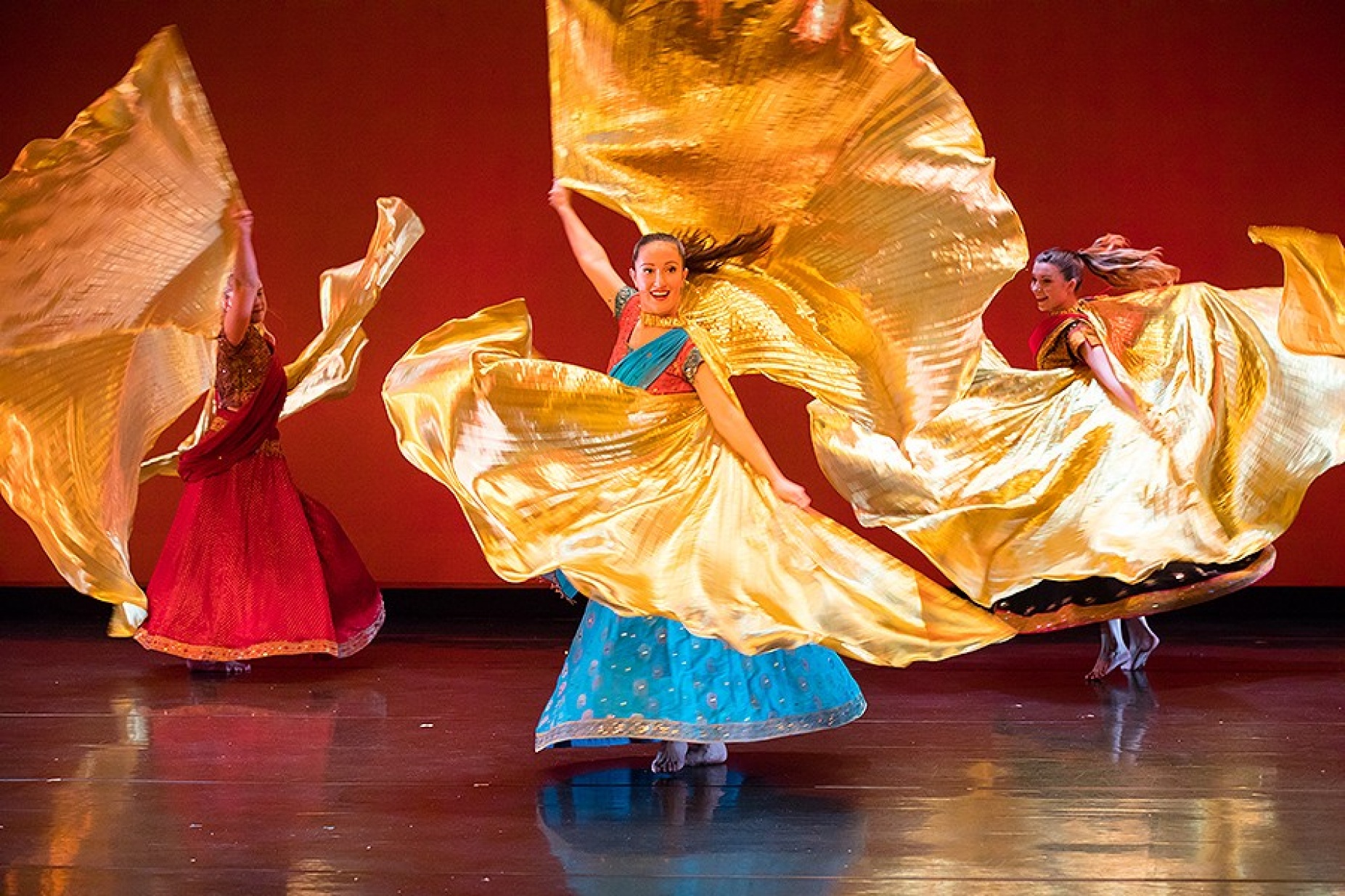 Zodiaque Dance Company - dancers on stage in brightly colored dresses with swirling golden flags. 