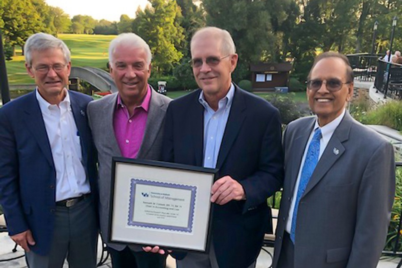 Kenneth W. Colwell and David Pfeil holding a plaque and standing with UB President Satish Tripathi and UB Provost Charles Zukoski at a golf course.