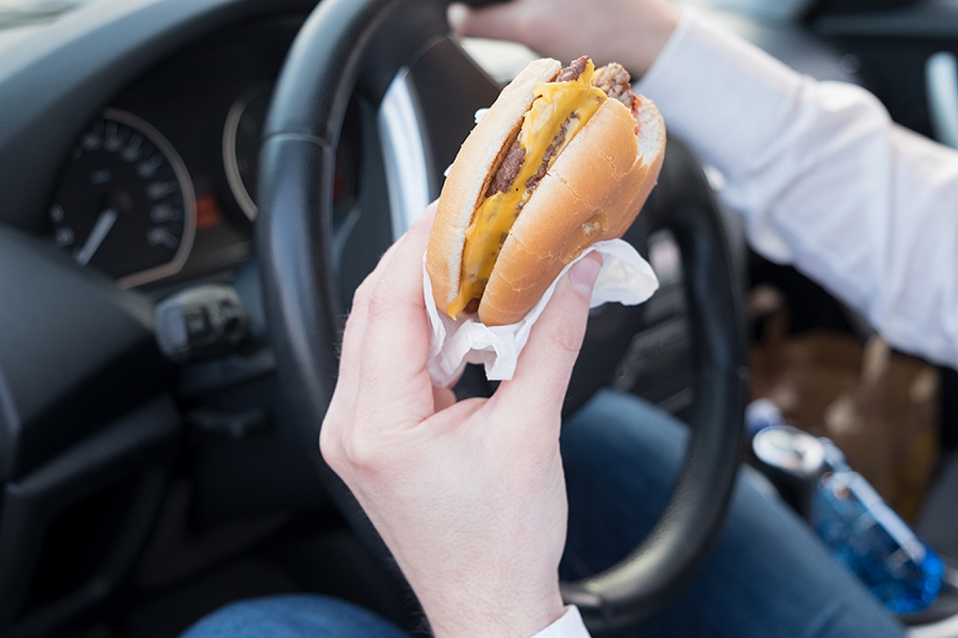 Person eating a fast food cheeseburger while driving.