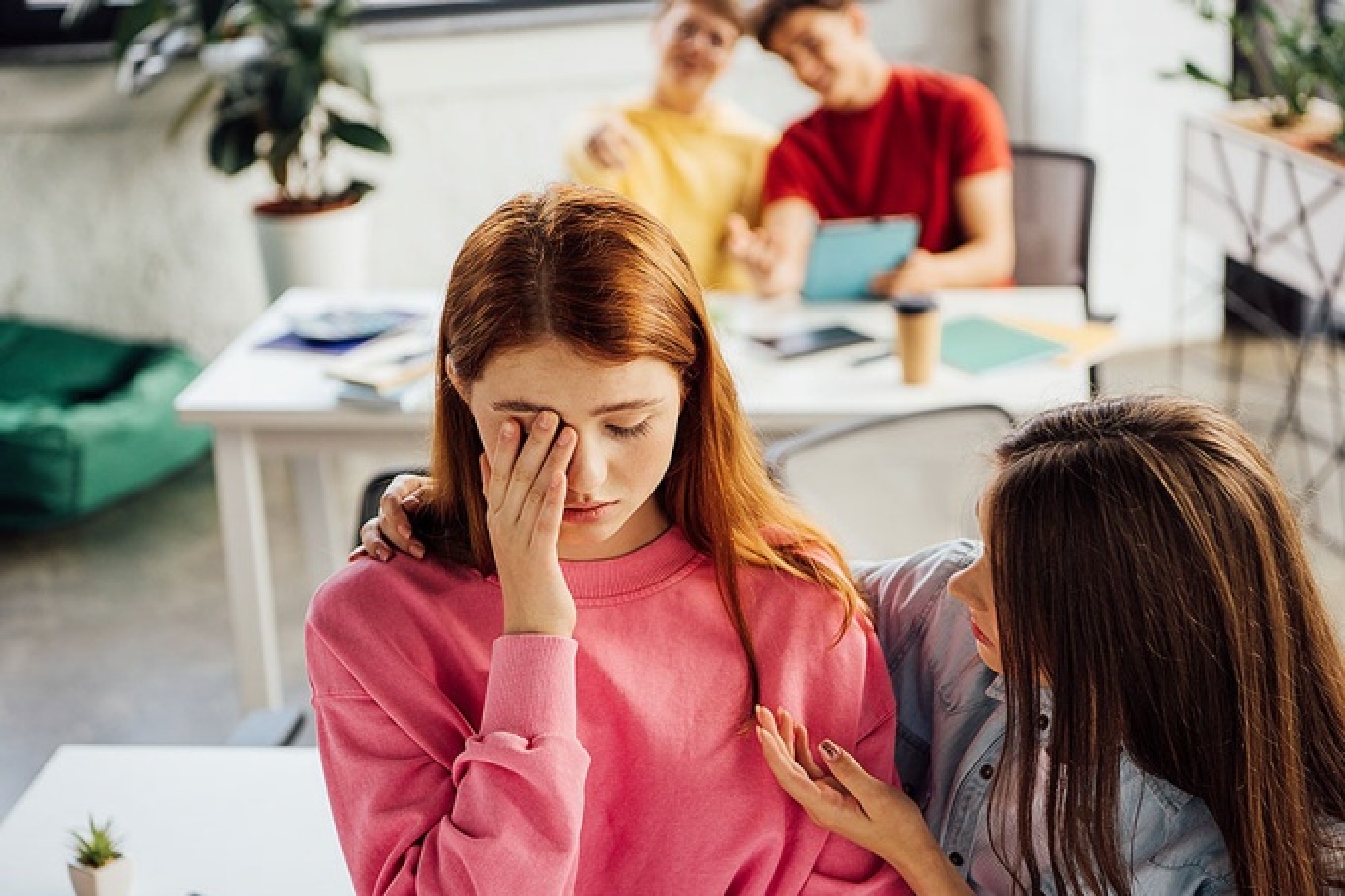 Teen girl supporting sad crying friend in school setting. 