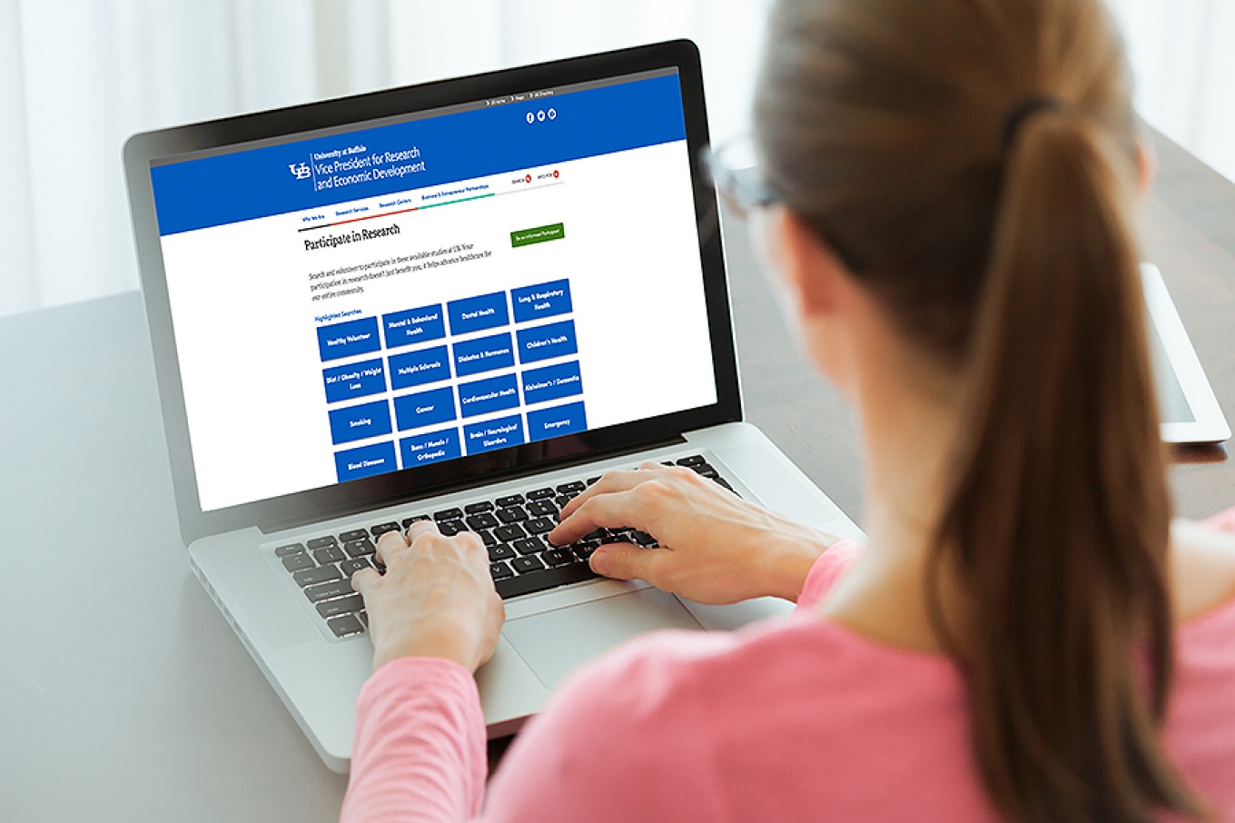 A woman looks at a computer screen displaying the Participate in Research Portal. 
