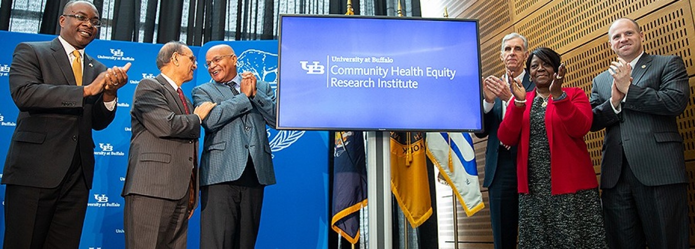 Photo of UB officials and elected leaders flanking a monitor that reads "University at Buffalo Community Health Equity Research Institute.".