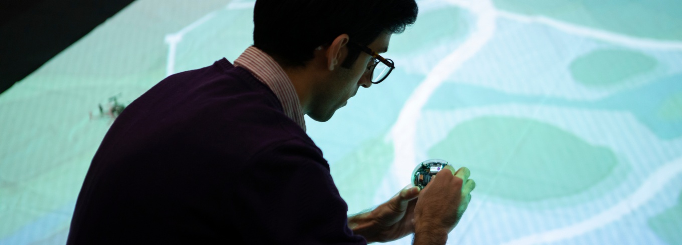 UB student works with mini-autonomous robot in front of a projected simulation of a city. 