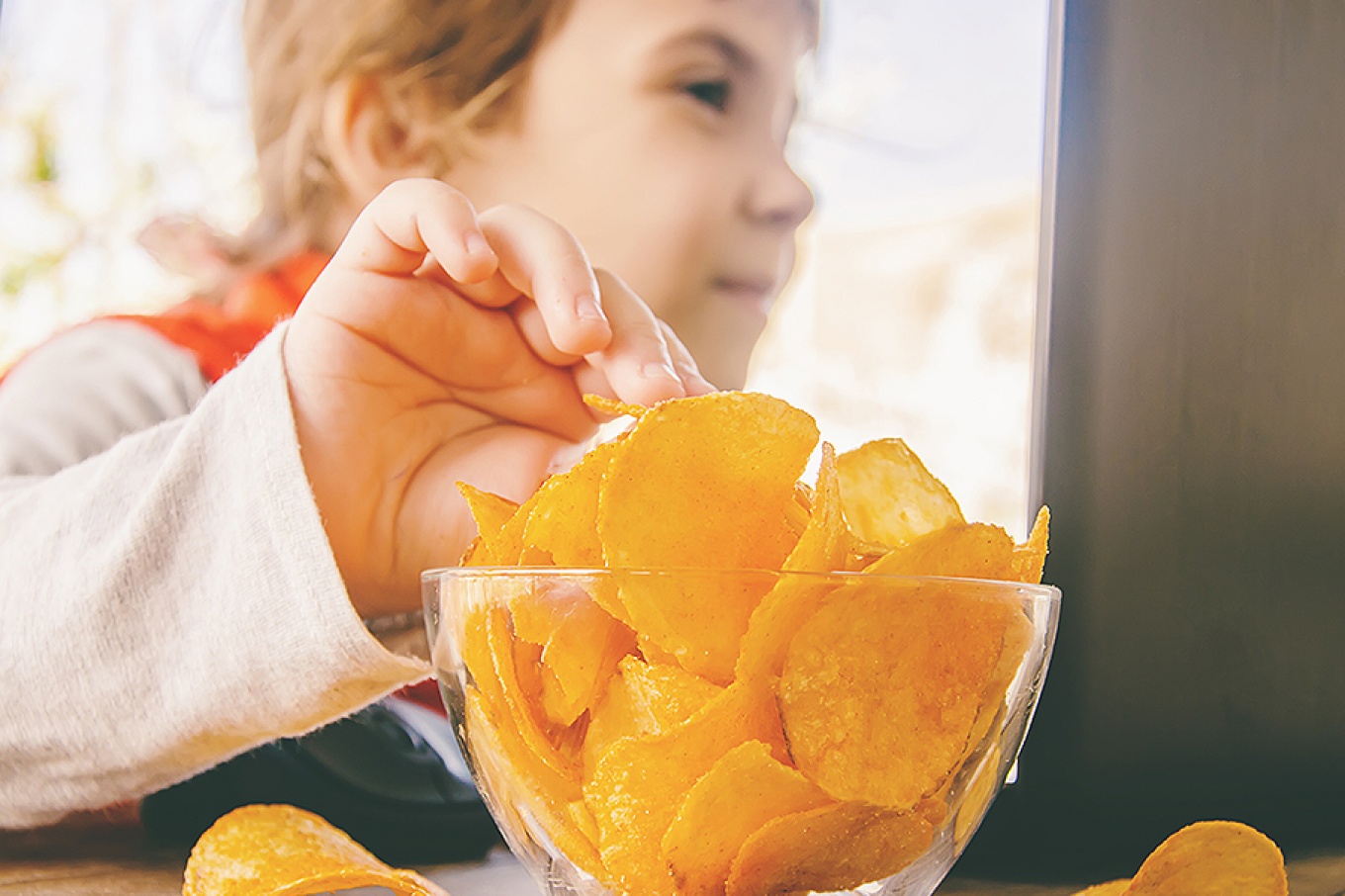 Child with chips behind a computer. 